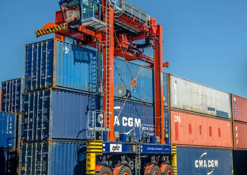 Container straddle carrier travelling between stacked containers in a port yard