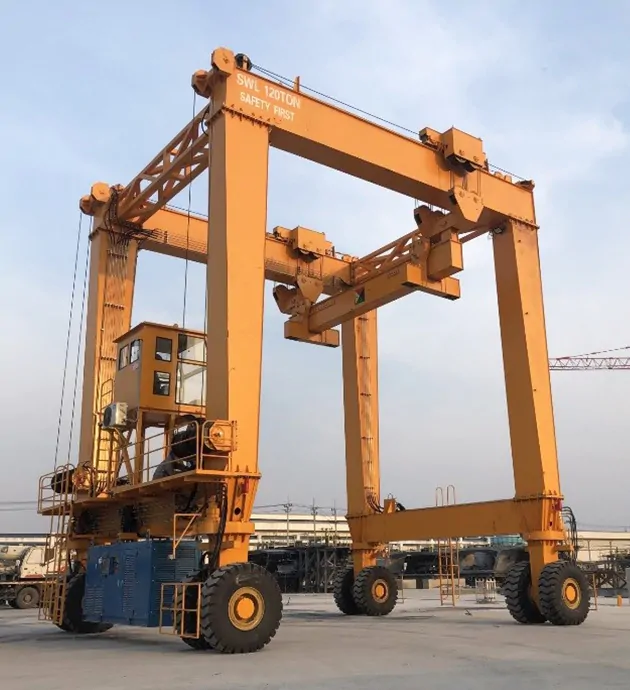 Orange industrial rubber-tired straddle carrier crane in a heavy equipment yard