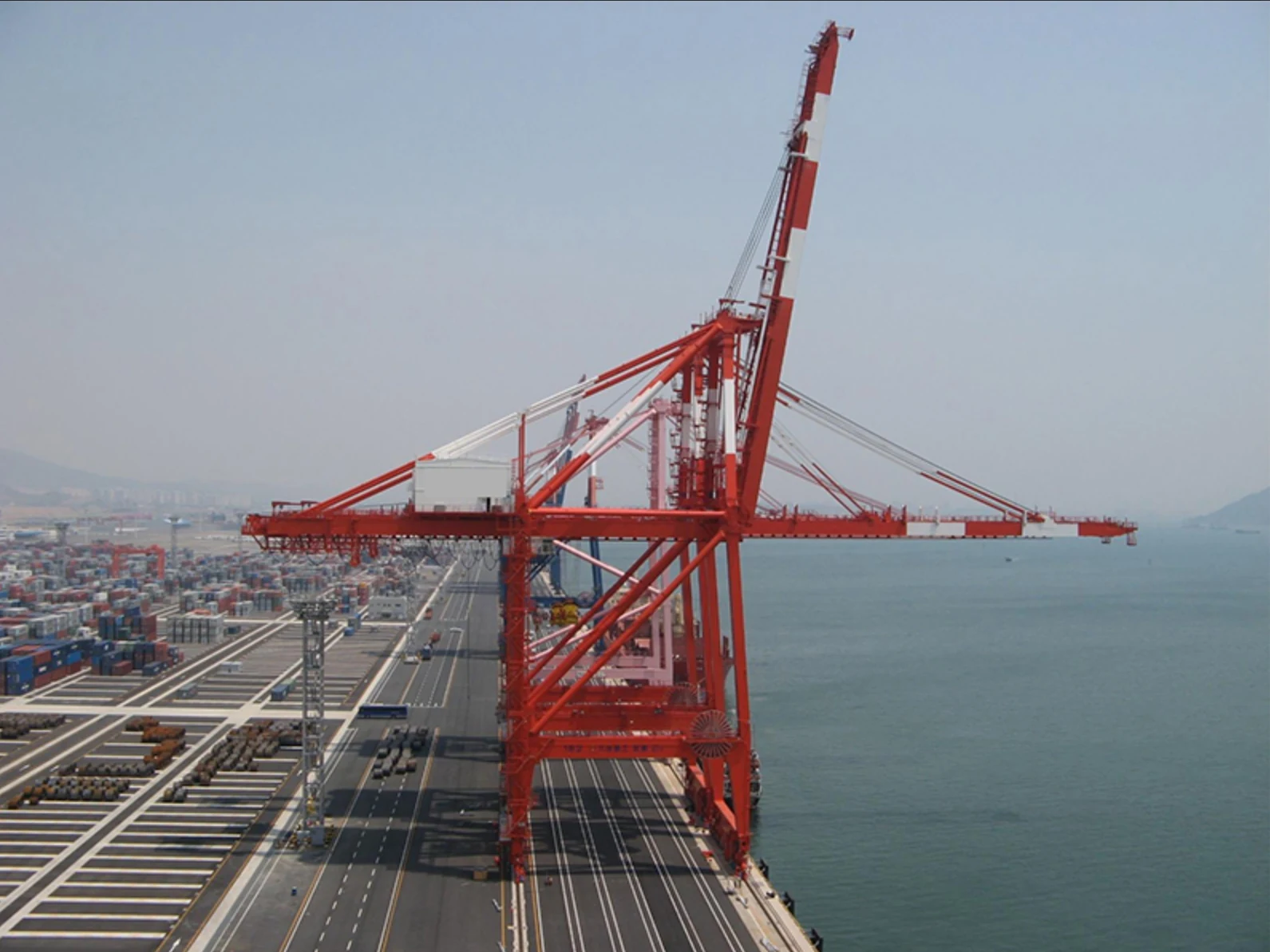Red rail-mounted ship-to-shore cranes along a container quay with one waterside boom raised