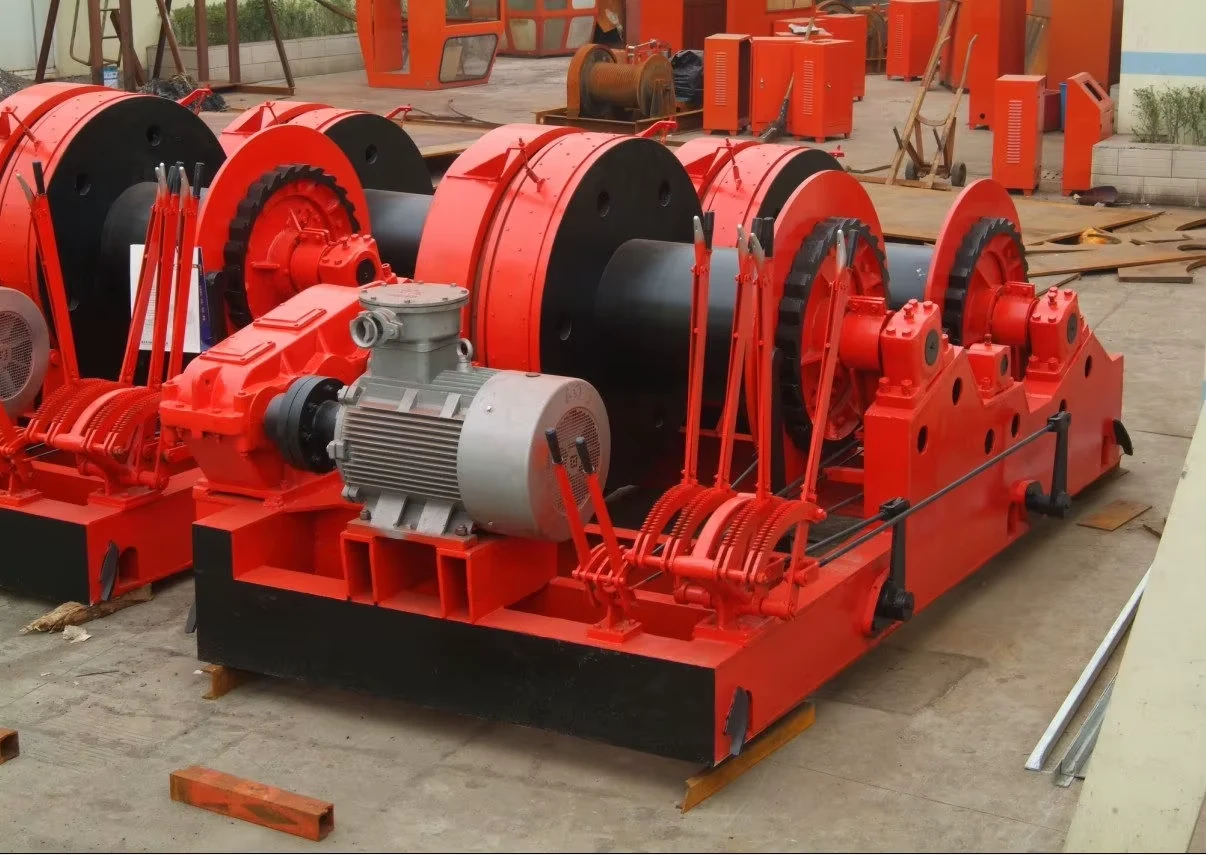 Red double-drum electric winch assemblies photographed in a workshop yard