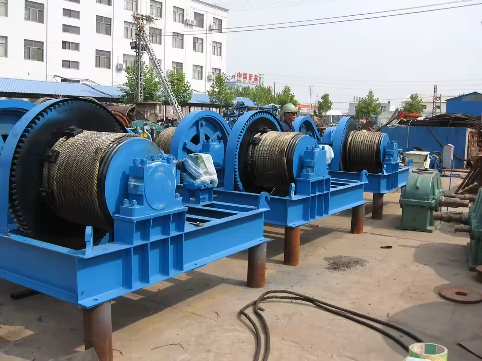 Several blue JM-series single-drum wire rope winches in a factory yard