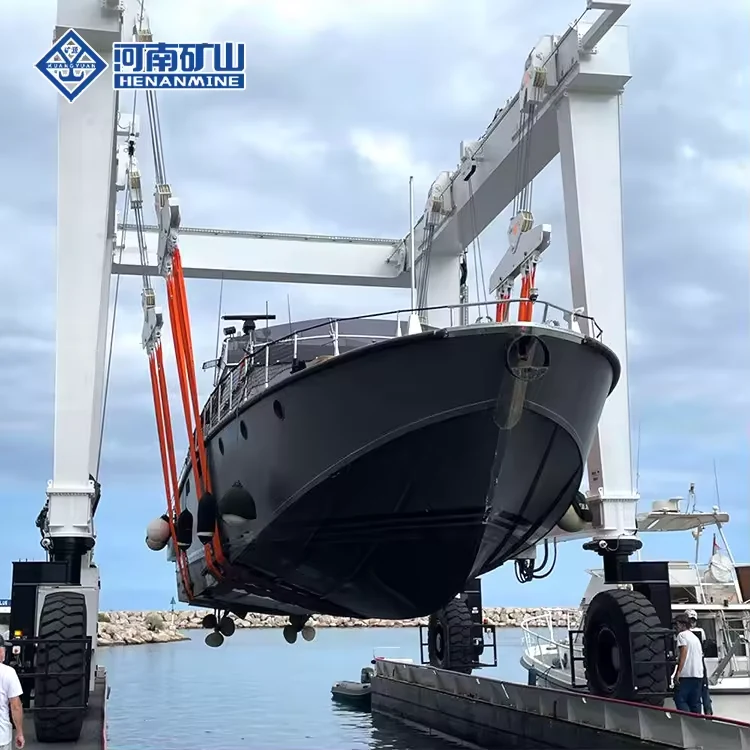 White mobile boat hoist lifting a dark-hulled yacht beside water