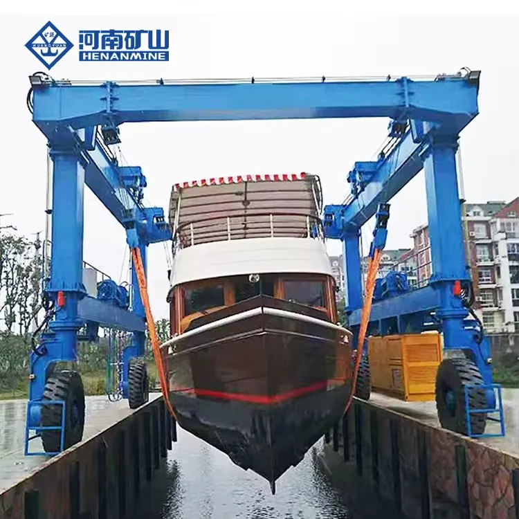 Complete blue rubber-tyred marine travel lift carrying a vessel in broad slings at a launch basin
